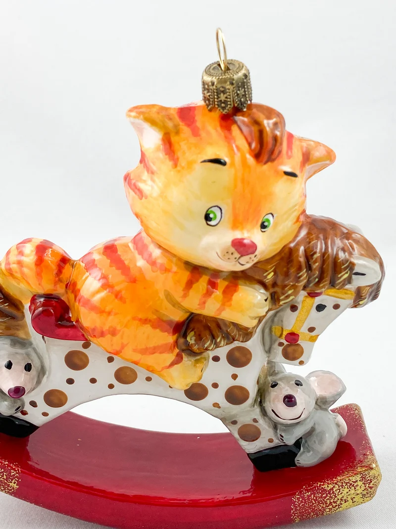 Die rote Tiger-Katze reitet auf dem getupften Schaukel-Pferdchen AtlasArt
