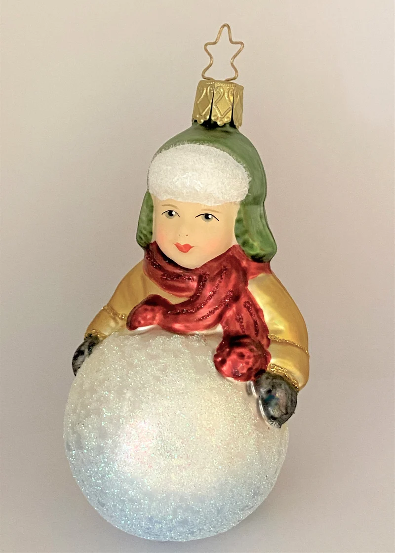 Kleiner Junge mit grüner Wintermütze macht einen riesigen Schneeball