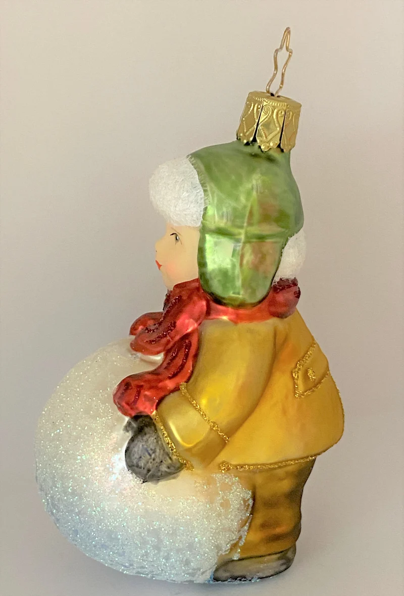 Kleiner Junge mit grüner Wintermütze macht einen riesigen Schneeball
