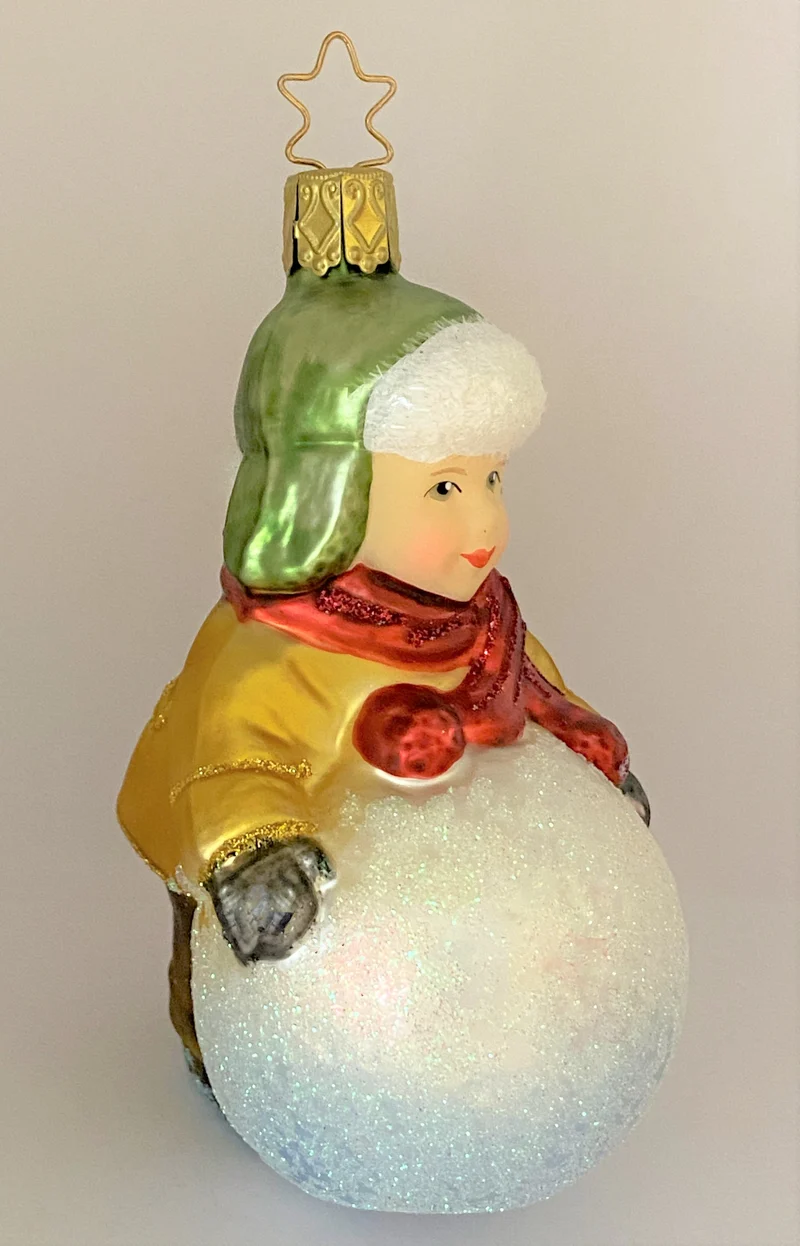 Kleiner Junge mit grüner Wintermütze macht einen riesigen Schneeball