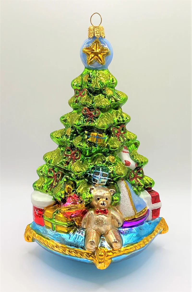 Christbaum mit Teddybär, Lokomotive und Segelboot auf blauem Kissen