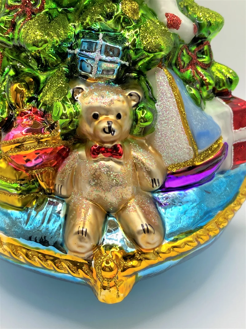 Christbaum mit Teddybär, Lokomotive und Segelboot auf blauem Kissen