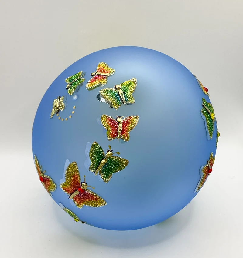 Transparente hellblaue Kugel mit strukturiert gemalten Schmetterlingen und metallenen Schmetterling